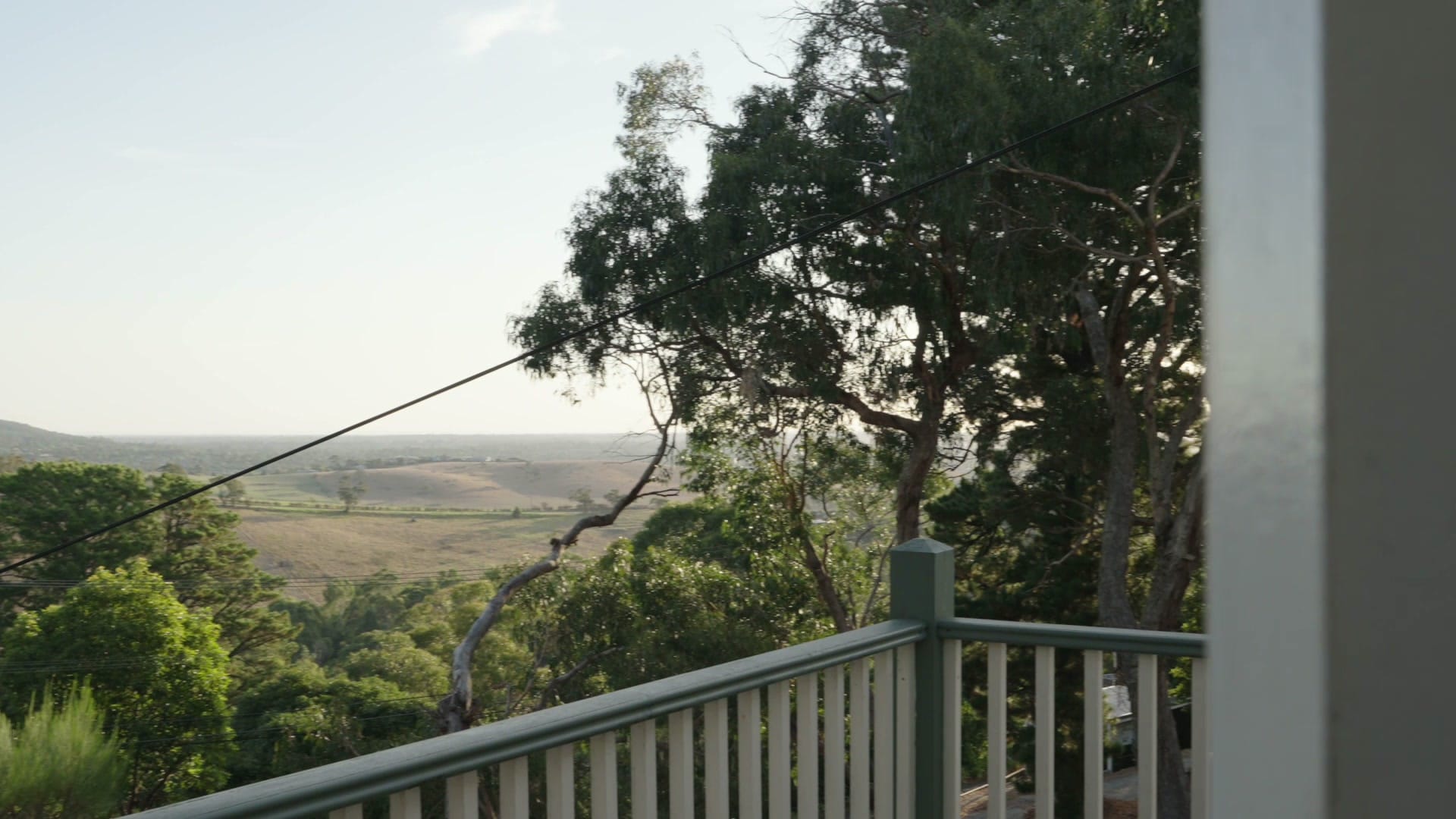 Golden-hour view from the deck at 9 Fern Road across gum trees to the plains beyond