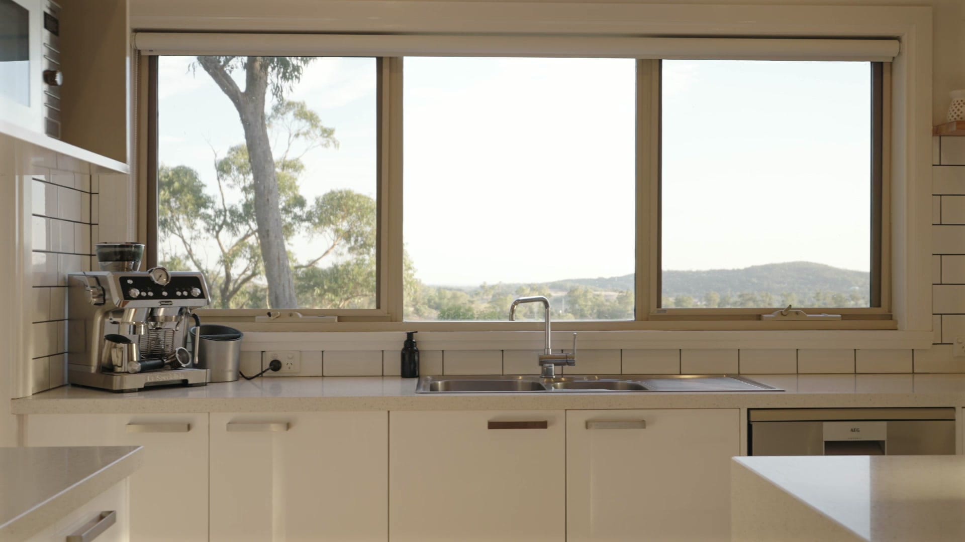 White kitchen with a wide window framing treetops and distant hills