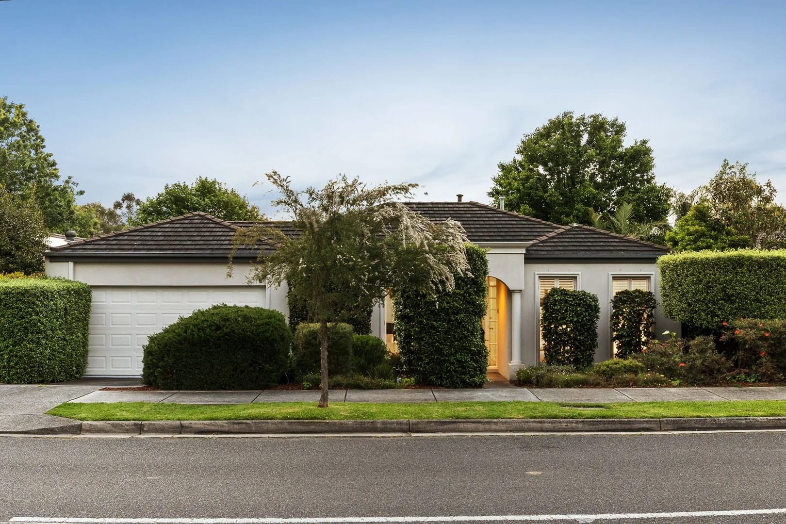 The front of 14 Willow Road, Upper Ferntree Gully, at dusk: a rendered single-storey home behind clipped hedges